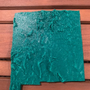 Peut inclure: Une carte en relief de l'état du Nouveau-Mexique, imprimée en 3D, en plastique vert turquoise. La carte est en relief et texturée pour montrer la topographie de l'état.