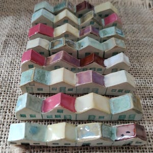 May include: A row of miniature ceramic houses with colorful glazed roofs and white walls. The houses are arranged in a staggered pattern, creating a whimsical and charming display.