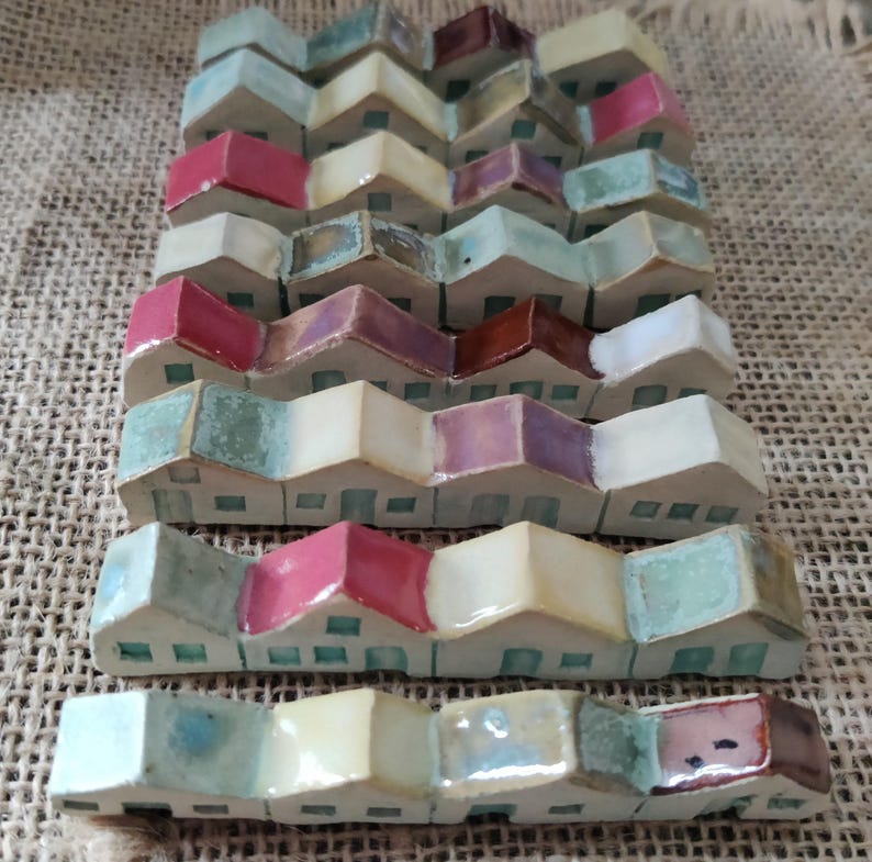 May include: A row of miniature ceramic houses with colorful glazed roofs and white walls. The houses are arranged in a staggered pattern, creating a whimsical and charming display.