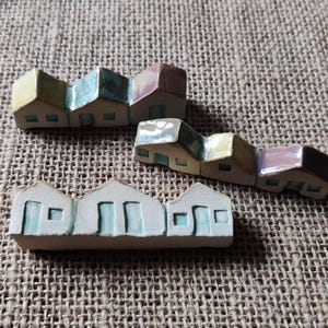 May include: A set of three miniature ceramic houses with colorful glazed details. The houses are arranged in a row and have a whimsical, handcrafted look.