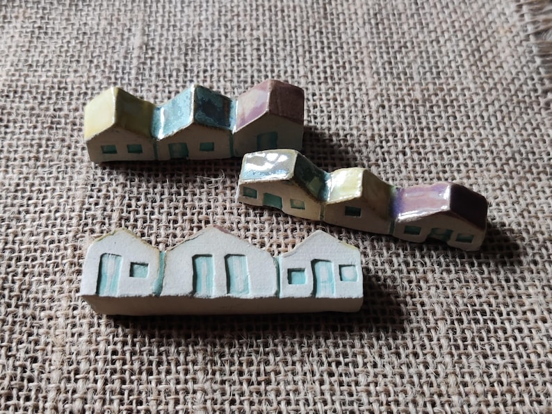 May include: A set of three miniature ceramic houses with colorful glazed details. The houses are arranged in a row and have a whimsical, handcrafted look.