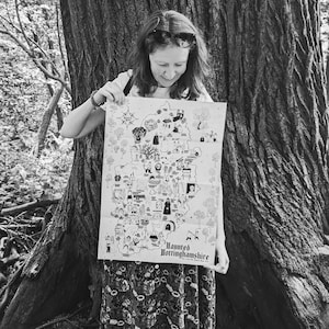 May include: A black and white illustrated map titled Haunted Nottinghamshire, featuring various small drawings of figures and landmarks across the county, printed on a rectangular sheet of paper held up to display the detailed graphic design.