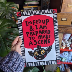 Puede incluir: Una impresión en blanco y negro con un globo de diálogo rojo que dice "I'm Fed Up & I Am Prepared To Make A Scene". Una criatura de dibujos animados negra con ojos amarillos está dentro del globo de diálogo.