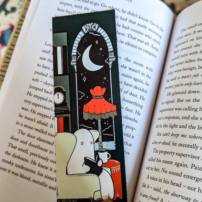 K&ouml;nnte beinhalten: Ein schwarz-wei&szlig;es Lesezeichen mit einem Geist, der auf einem Stuhl ein Buch liest. Der Geist ist wei&szlig; mit schwarzem Umriss. Der Hintergrund ist ein dunkler Raum mit einem roten Lampenschirm und einem Halbmond im Fenster.