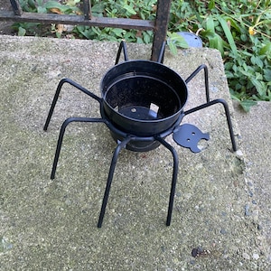 May include: Black metal spider plant stand with a black plastic pot. The spider stand has eight legs and a small black spider head.