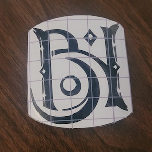 May include: A black vinyl decal with the letters "Bi" in a stylized font. The decal is on a white sheet with a grid pattern.
