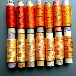 May include: A collection of 10 spools of thread, with a mix of orange and gold colors. The spools are labeled with numbers and letters.