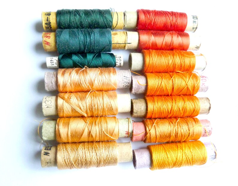 May include: A collection of spools of thread in various shades of orange, green, and red. The spools are wrapped in paper with printed labels and numbers.