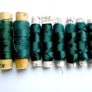 May include: Eight spools of dark green thread, each wrapped in paper with the text "50 Meter", "Kunst Seide", "WZ", "FA", and "453" printed on them.
