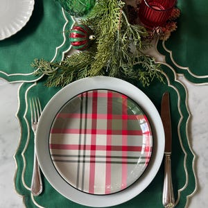 Può includere: Un piatto bianco con bordo nero e un design a quadri in rosso, verde e bianco. Il piatto è su un sottopiatto verde con bordi a festoni.