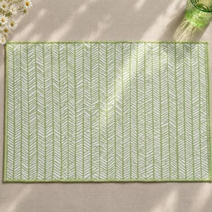May include: A rectangular placemat featuring a light green and white herringbone pattern. The design consists of vertical columns of repeating chevron shapes with a textured appearance, finished with a matching green stitched border edge.