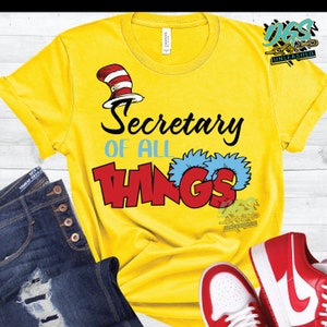 May include: Yellow t-shirt with a red and white cat hat and the text "Secretary of all things" in red and blue letters.