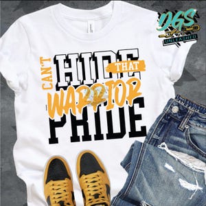 Op de afbeelding: Wit T-shirt met zwarte tekst die "Can't Hide That Warrior Pride" luidt. De tekst is in een vetgedrukt, graffiti-achtig lettertype. Een gele en zwarte afbeelding van een krijger bevindt zich in het midden van de tekst. Het shirt ligt op een oppervlak met een paar zwart-gele sneakers en een blauwe jeans.