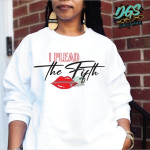 Op de afbeelding: Wit sweatshirt met de tekst "I Plead the Fifth" in zwarte en rode letters. Een rode mond met een rits is afgebeeld met de tekst.