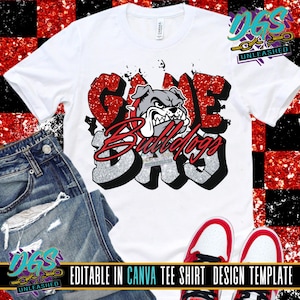 May include: White t-shirt featuring a graphic design with the words "GAME DAY" in red glitter and silver lettering, along with a bulldog mascot. The shirt is paired with blue jeans and red and white sneakers.