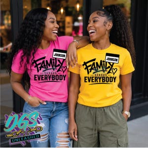 May include: A bright pink t-shirt and a bright yellow t-shirt, both featuring black graphic text that reads FAMILY VERSUS EVERYBODY and a small name tag graphic that says JOHNSON. Each shirt includes a small heart icon near the text.