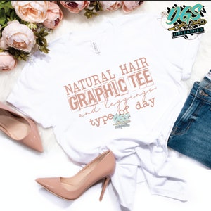 Puede incluir: Camiseta blanca con el texto "NATURAL HAIR GRAPHIC TEE and leggings type of day" en texto marrón con un diseño floral.