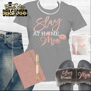 May include: A gray t-shirt with the text "Slay at Home Mom" in rose gold glitter. The shirt is paired with a rose gold glitter notebook, a pen, a mug with the same text, and a pair of gray fuzzy slippers with the text "Slay at Home" and "Mom" in rose gold glitter.