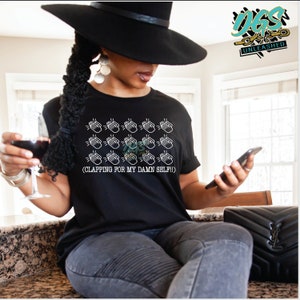 May include: Black t-shirt with a white graphic of multiple clapping hands and the text "(CLAPPING FOR MY DAMN SELF!)"