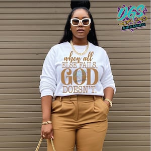 May include: White long-sleeve sweatshirt with the text "when all ELSE FAILS, GOD DOESN'T." printed in brown. The model is wearing brown pants and a gold necklace.