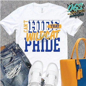 Puede incluir: Camiseta blanca con texto azul y amarillo que dice "Can't Hide That Wildcat Pride". La camiseta se combina con jeans azules, zapatillas blancas y una bolsa de mano amarilla y azul.