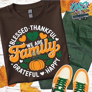 May include: A brown t-shirt with the words "Blessed, Thankful, We Are Family, Grateful, Happy" in a circular design with orange and green accents. The image also includes green cargo pants and orange and white sneakers.