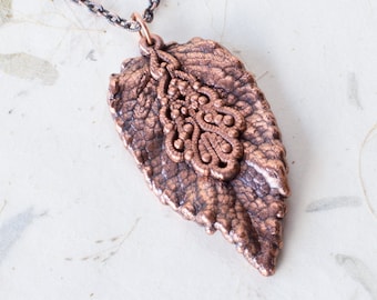 May include: A copper leaf pendant necklace with a detailed filigree design. The pendant is attached to a silver chain.