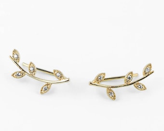 May include: A pair of gold leaf earrings with small clear stones. The earrings are shaped like a branch with leaves.