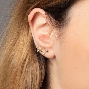 May include: A gold ear cuff with a delicate branch design and small clear stones. The ear cuff is worn on the upper part of the ear.