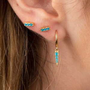 May include: A pair of gold earrings with turquoise stones. One earring is a small bar with turquoise stones, and the other is a hoop with a turquoise stone dangle.