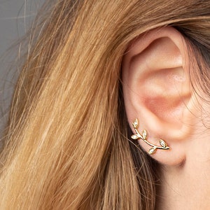 May include: Gold leaf ear cuff with small clear stones. The ear cuff is shaped like a branch with leaves.