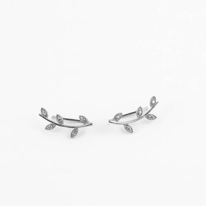May include: A pair of silver ear climbers with a delicate leaf design. Each climber features a branch with five leaves, each leaf adorned with a small, clear crystal.