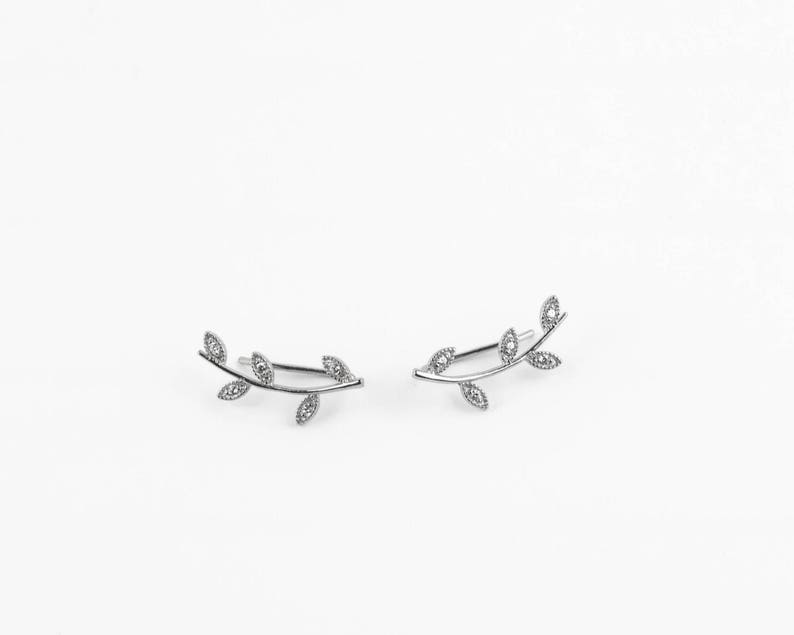 May include: A pair of silver ear climbers with a delicate leaf design. Each climber features a branch with five leaves, each leaf adorned with a small, clear crystal.