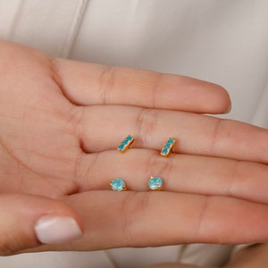 May include: A set of four gold earrings with turquoise stones. Two earrings are small round stones and two earrings are thin bars with three stones each.