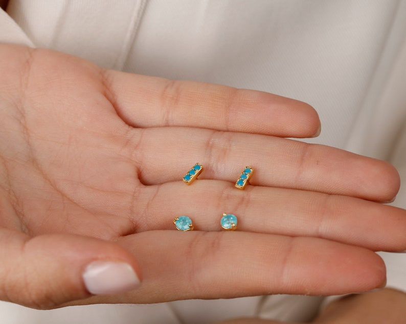 May include: A set of four gold earrings with turquoise stones. Two earrings are small round stones and two earrings are thin bars with three stones each.