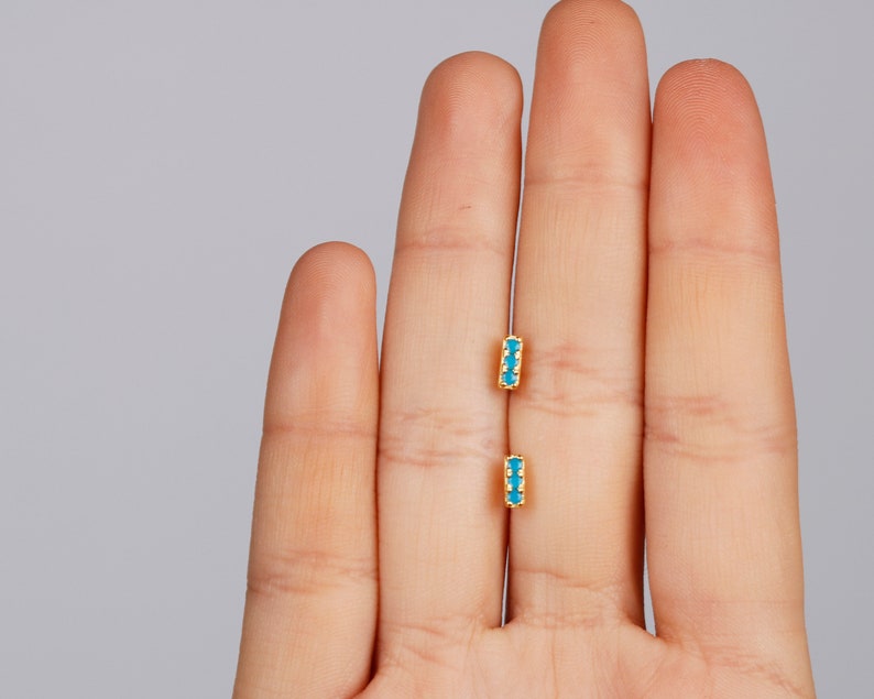May include: A pair of gold earrings with small turquoise stones set in a bar shape.
