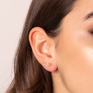 May include: A pair of gold leaf earrings. The earrings are small and delicate, and they feature a design of a branch with leaves.