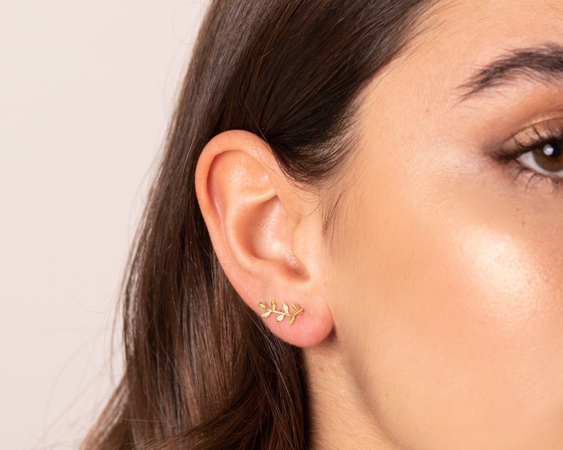 May include: A pair of gold leaf earrings. The earrings are small and delicate, and they feature a design of a branch with leaves.