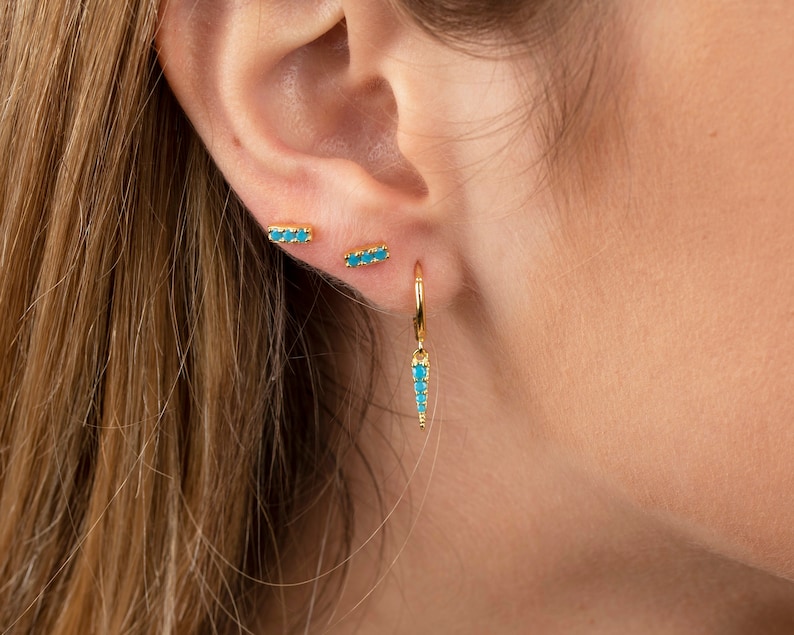 May include: A pair of gold earrings with turquoise stones. One earring is a small bar with turquoise stones, and the other is a hoop with a turquoise stone dangle.