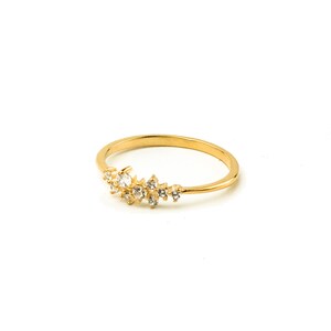 May include: A gold ring with a delicate design of small, clear stones set in a curved line.