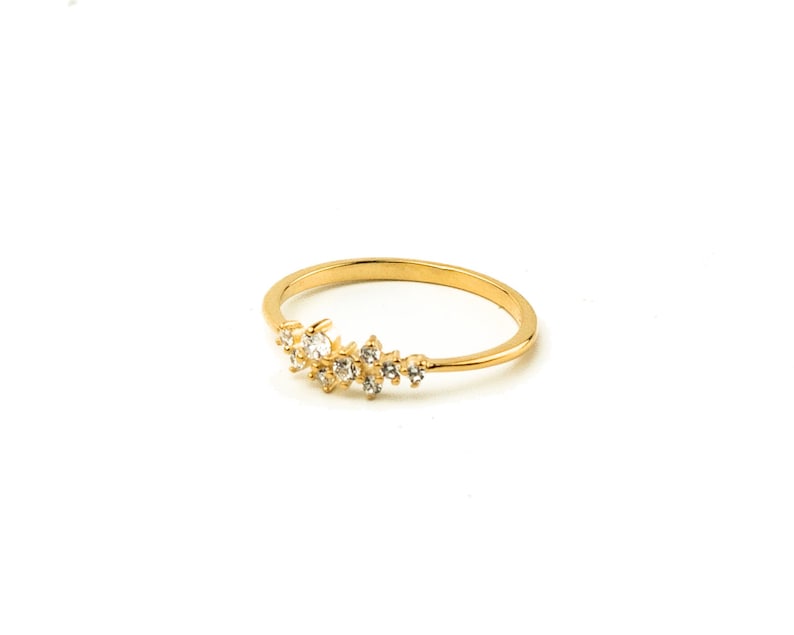 May include: A gold ring with a delicate design of small, clear stones set in a curved line.