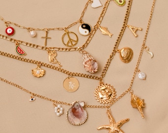 Pode incluir: Um conjunto de colares de corrente de ouro com vários pingentes, incluindo um sinal de paz, uma cruz, uma melancia, uma concha, um sol, uma estrela do mar, uma lua crescente, um abacate, um peixe, um símbolo yin yang, um mau-olhado, um coração e uma letra A.