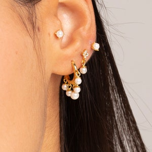 May include: Gold hoop earrings with dangling pearls and a small gold stud earring with a pearl