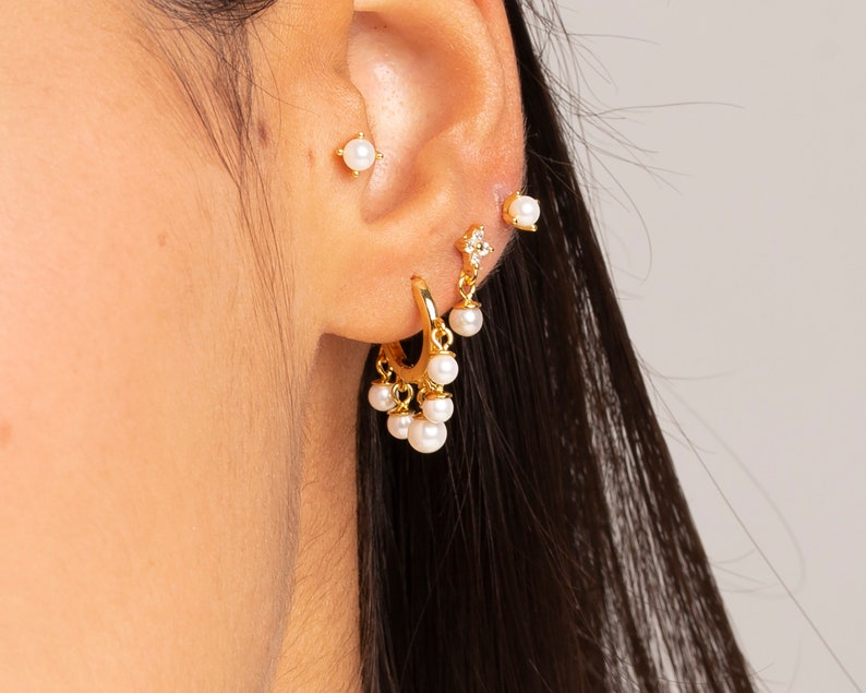 May include: Gold hoop earrings with dangling pearls and a small gold stud earring with a pearl