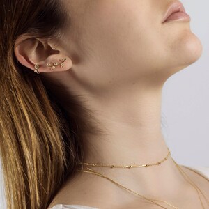 May include: A woman wearing a gold chain necklace with a delicate gold chain choker. The choker has small gold beads.