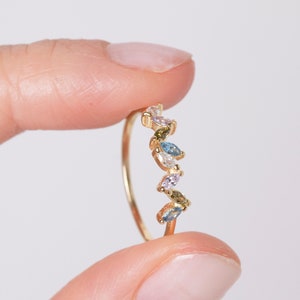 Può includere: Un anello d'oro con una fila di pietre preziose di forma marquise colorate. Le pietre preziose sono incastonate in un delicato design a forma di foglia.