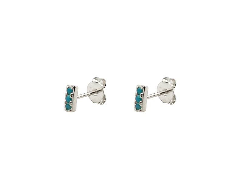 May include: A pair of silver stud earrings with a small turquoise bar set with five turquoise stones.