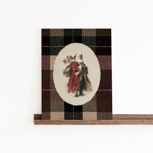 May include: An oval-shaped Christmas card featuring an illustration of Santa Claus carrying a sack of toys. The image is set against a plaid background in shades of brown, black, and burgundy. The card is displayed on a wooden shelf.