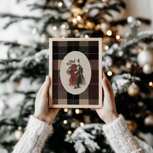 May include: A framed Christmas print featuring an oval image of Santa Claus carrying a sack. The print is set against a plaid background in shades of black, brown, and burgundy, with a wooden frame.