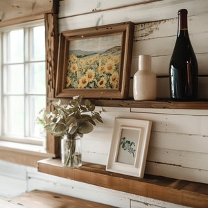 May include: Two wooden shelves with a white vase, a bottle of wine, a framed print of sunflowers, and a framed print of a botanical illustration.